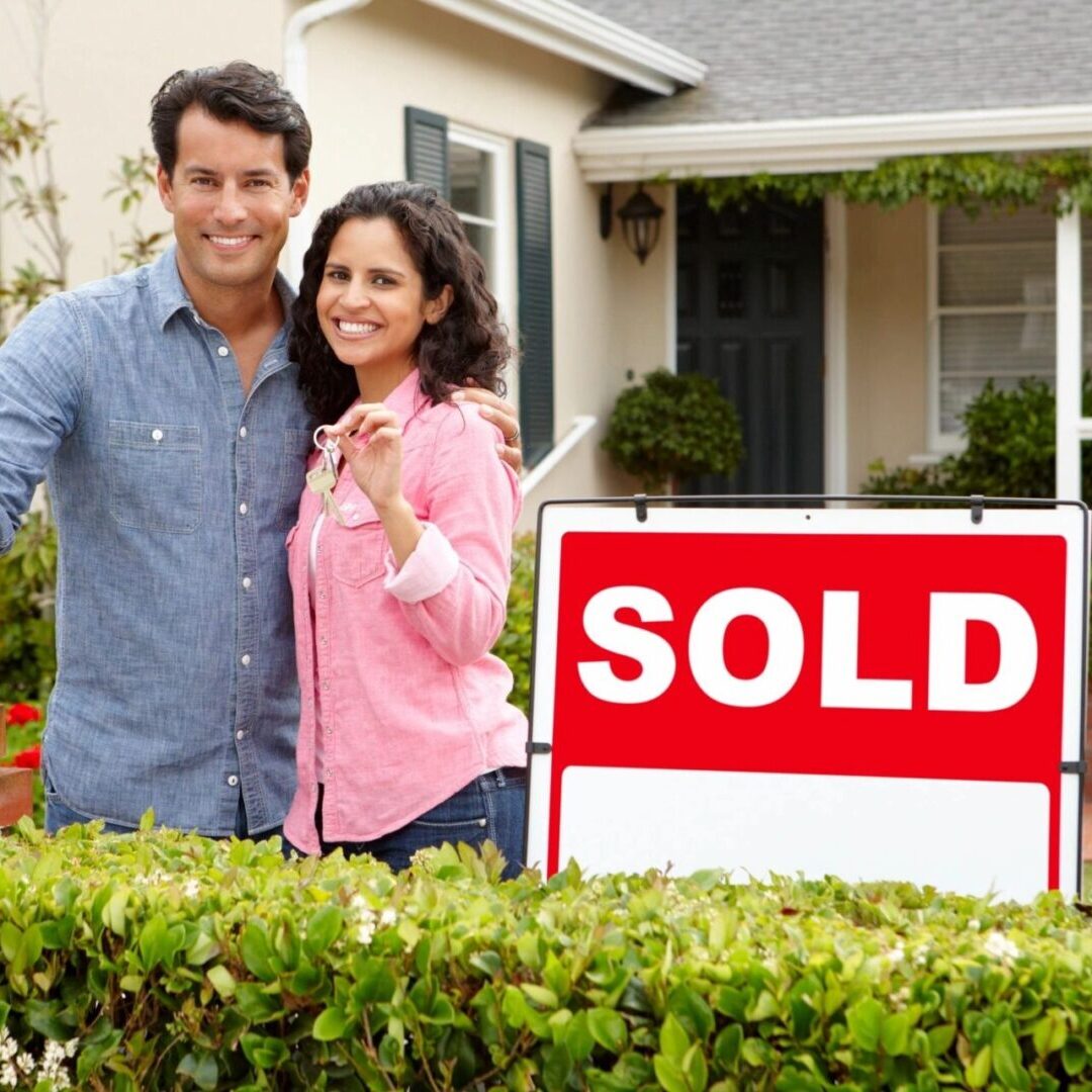 A couple standing in front of their home with the sold sign.
